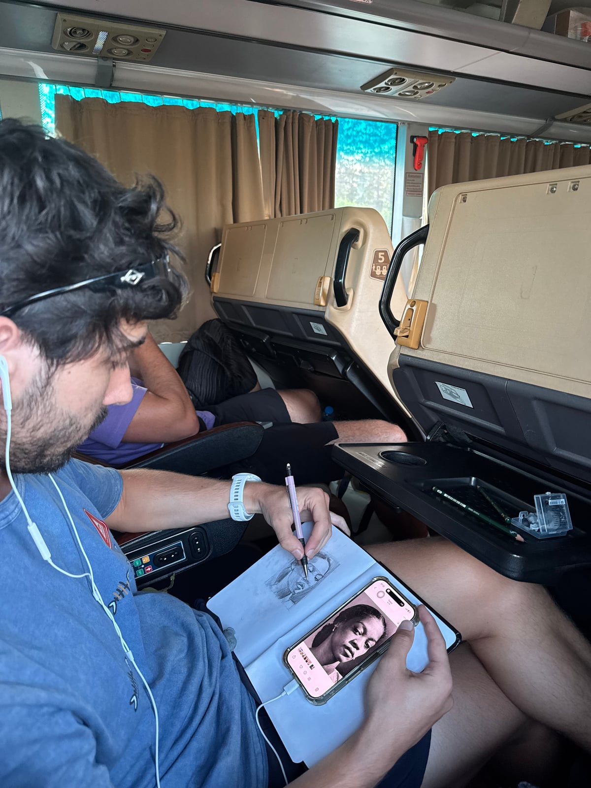 Yoav Mendelson sketching a portrait in a sketchbook on a bus.